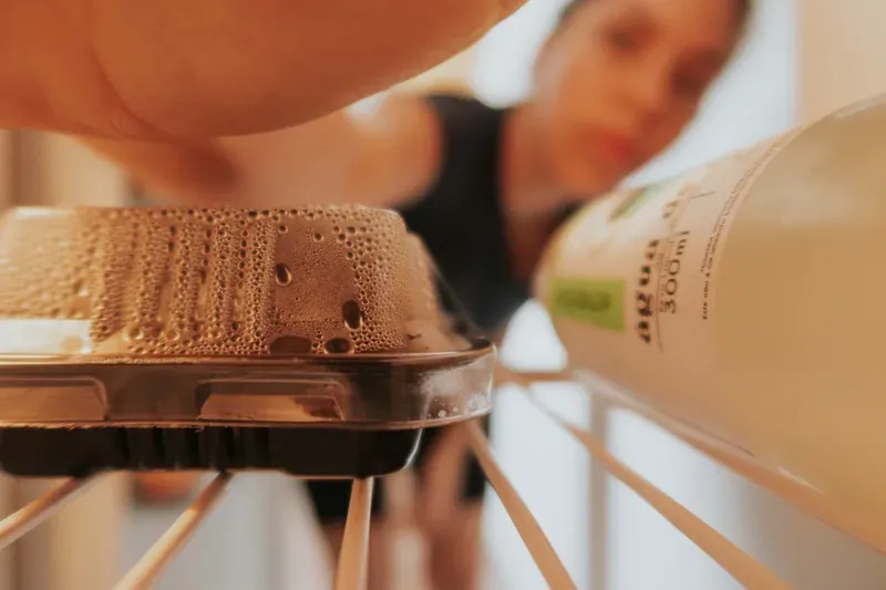 Hand lifting a condensation-covered plastic tray from a fridge shelf beside a bottle of water