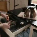 Woman lifting spoons from a grey cutlery tray in an open drawer beside a steel hob-top kettle