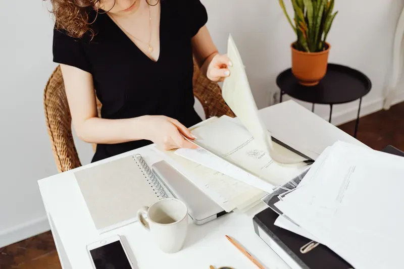 Woman in a black top lifting a sheet of paper from a pile of documents on a white desk