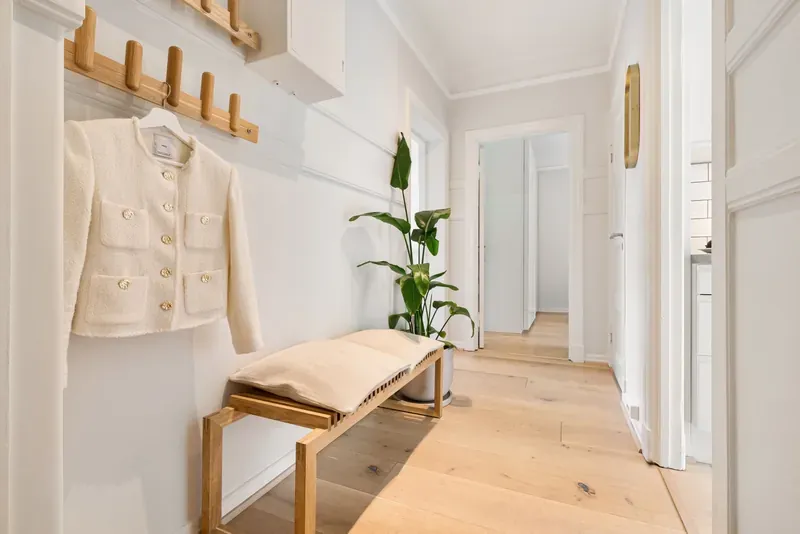 Cream jacket hanging on an oak peg rail above a slatted wooden bench in a white-painted hallway
