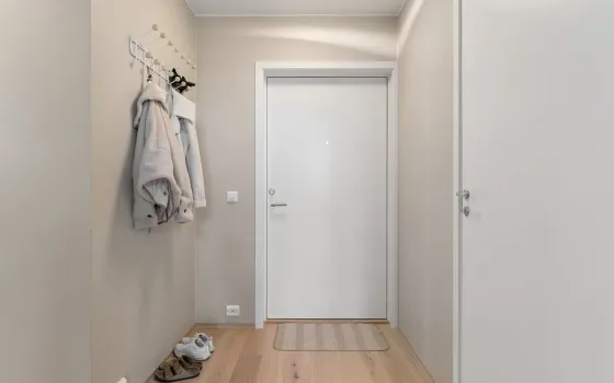 Narrow beige hallway with a white front door, two fleece jackets on wall hooks and trainers on the floor
