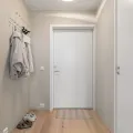 Narrow beige hallway with a white front door, two fleece jackets on wall hooks and trainers on the floor
