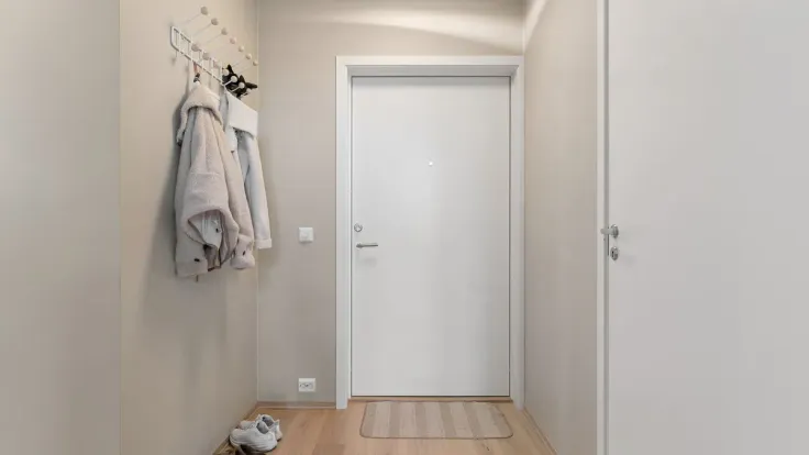 Narrow beige hallway with a white front door, two fleece jackets on wall hooks and trainers on the floor