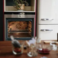Open empty electric oven showing its fan and two wire shelves, beside a cream retro fridge freezer