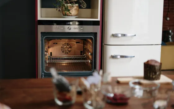 Open empty electric oven showing its fan and two wire shelves, beside a cream retro fridge freezer