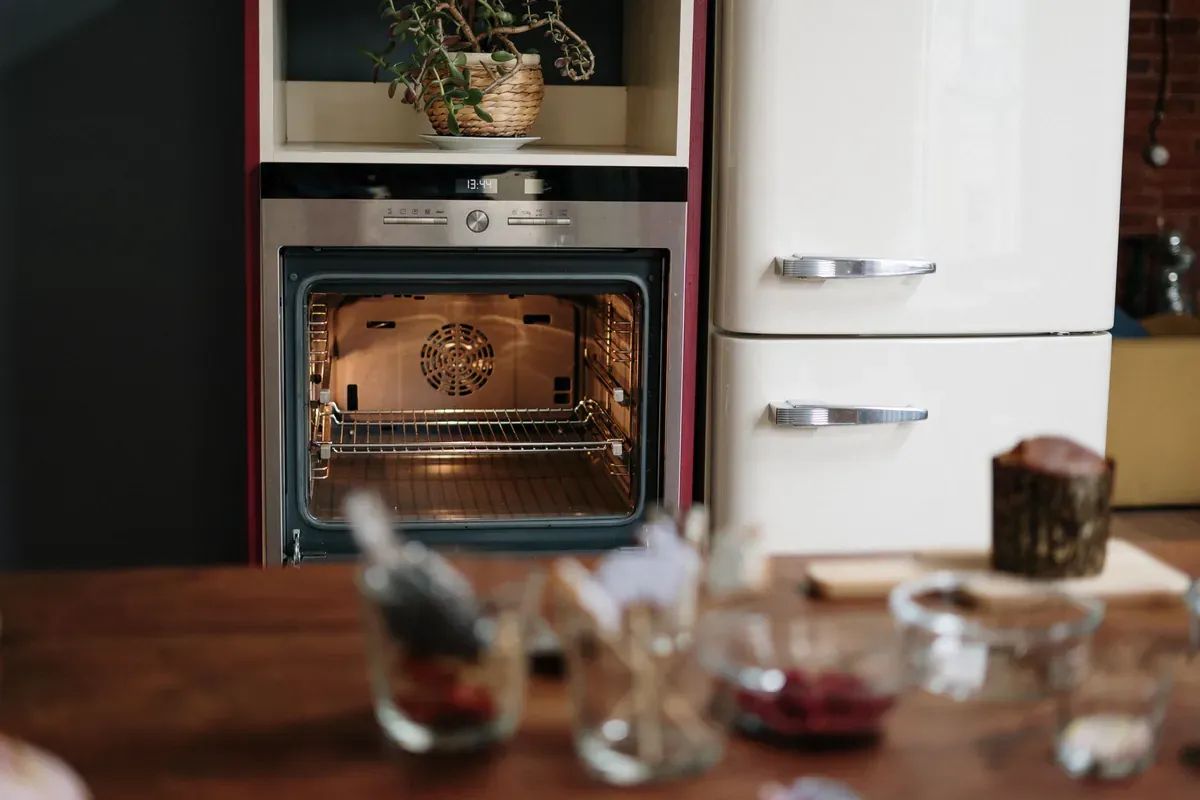 Open empty electric oven showing its fan and two wire shelves, beside a cream retro fridge freezer
