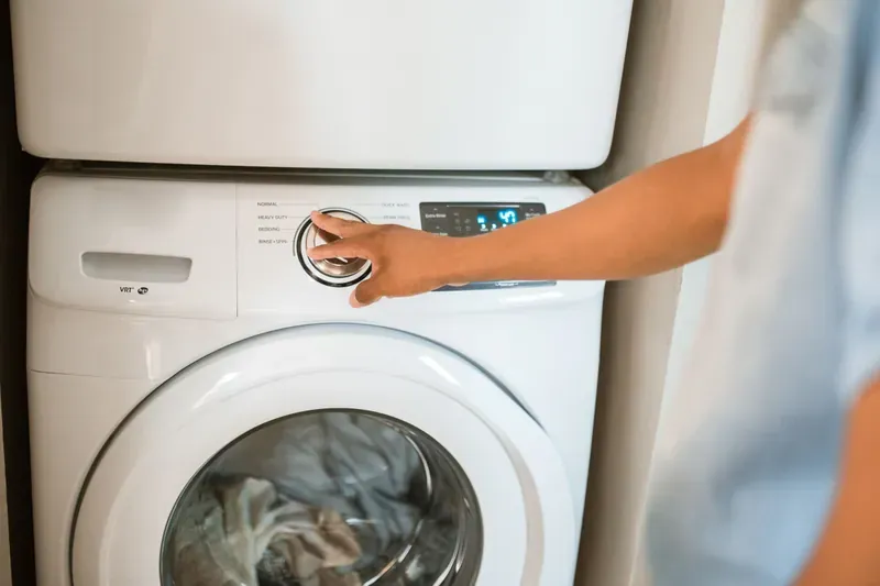 Hand turning the programme dial on a white front-loading washing machine with laundry visible through the door