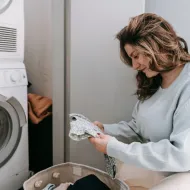 Woman sitting on the floor checking a patterned garment beside a stacked washer and dryer