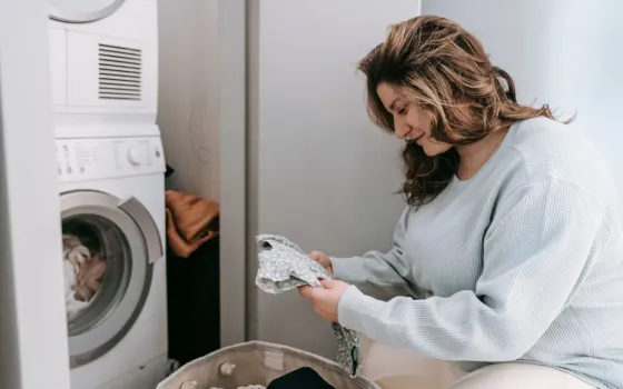 Woman sitting on the floor checking a patterned garment beside a stacked washer and dryer
