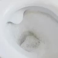 Looking down into a white ceramic toilet bowl as it flushes, with foam and swirling water in the trap