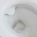 Looking down into a white ceramic toilet bowl as it flushes, with foam and swirling water in the trap