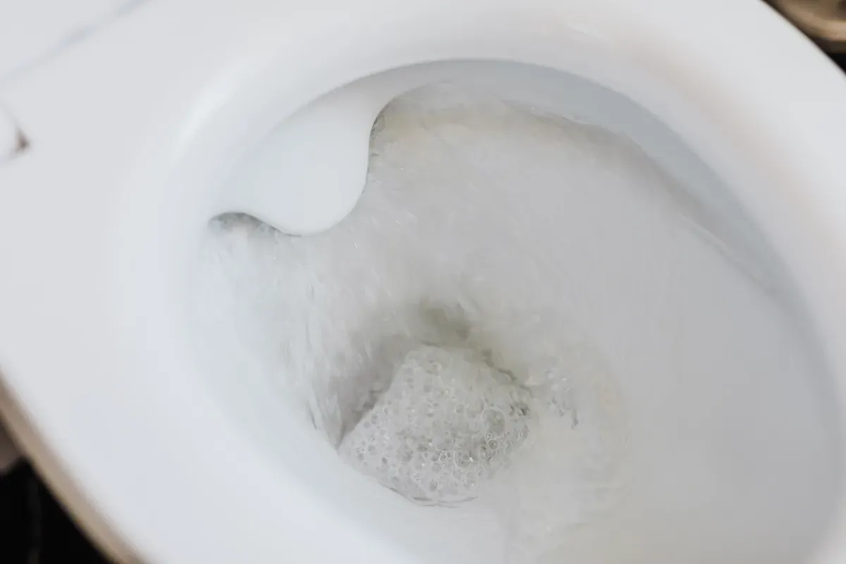 Looking down into a white ceramic toilet bowl as it flushes, with foam and swirling water in the trap