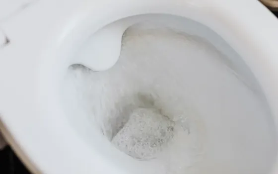 Looking down into a white ceramic toilet bowl as it flushes, with foam and swirling water in the trap