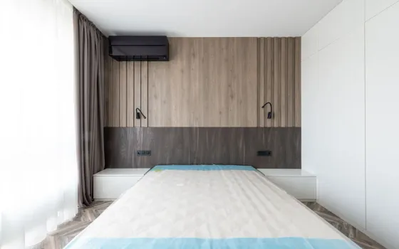 Bare double mattress with a blue-edged quilted top in a bedroom with slatted oak wall panelling and two black reading lights