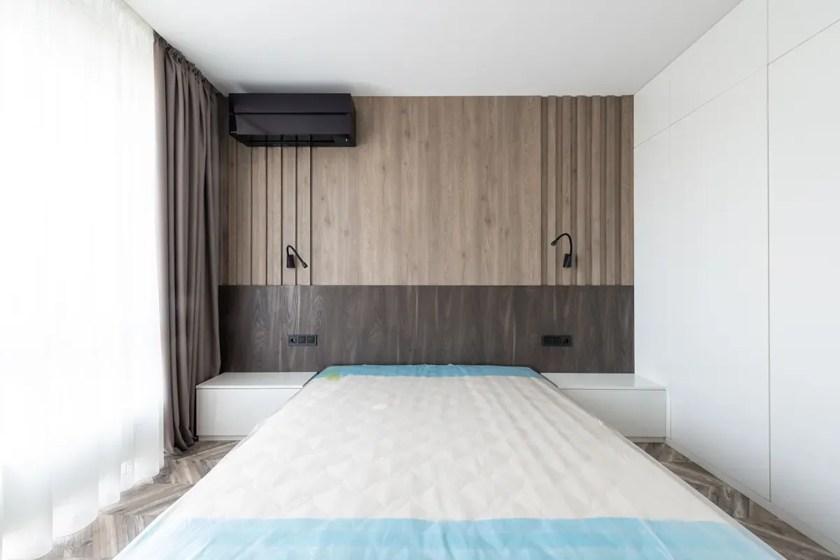 Bare double mattress with a blue-edged quilted top in a bedroom with slatted oak wall panelling and two black reading lights