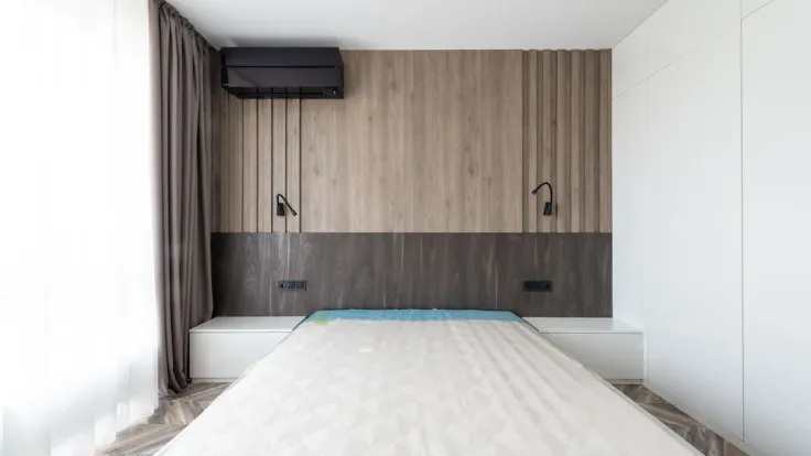 Bare double mattress with a blue-edged quilted top in a bedroom with slatted oak wall panelling and two black reading lights
