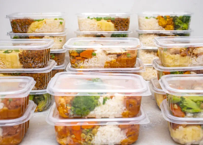 Rows of stacked clear plastic tubs of rice, broccoli and tomato sauce dishes on a white surface
