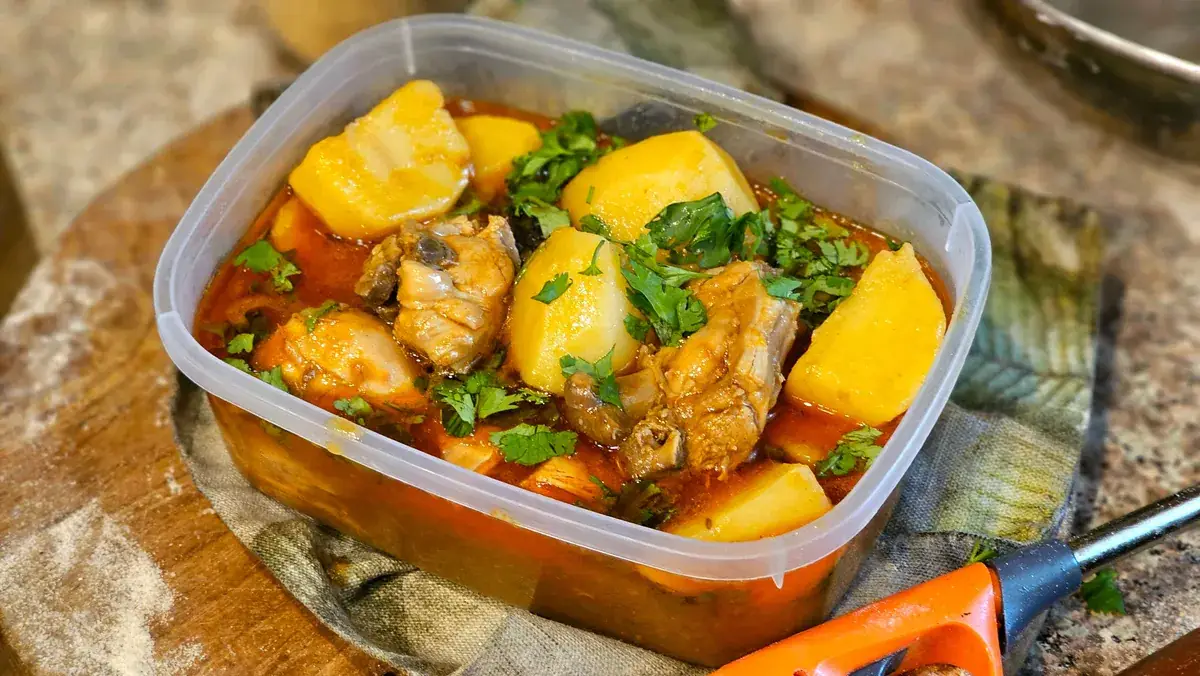 Chicken and potato stew with chopped coriander in a clear plastic tub on a floured wooden board