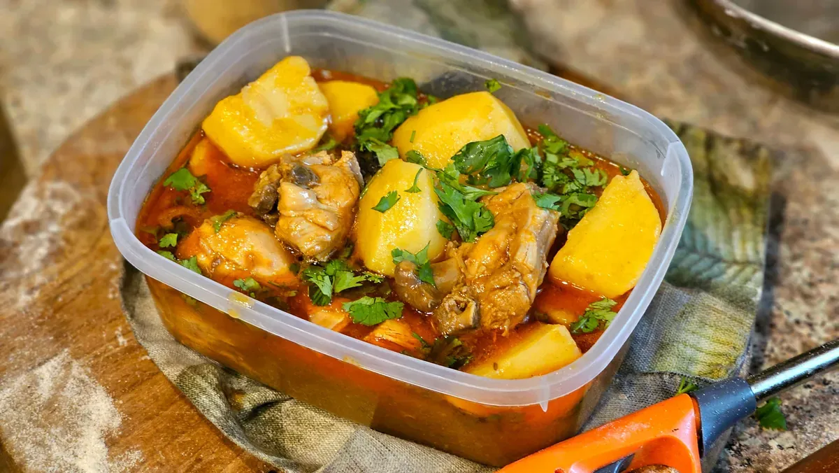 Chicken and potato stew with chopped coriander in a clear plastic tub on a floured wooden board
