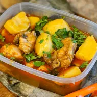 Chicken and potato stew with chopped coriander in a clear plastic tub on a floured wooden board