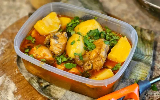 Chicken and potato stew with chopped coriander in a clear plastic tub on a floured wooden board