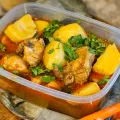 Chicken and potato stew with chopped coriander in a clear plastic tub on a floured wooden board