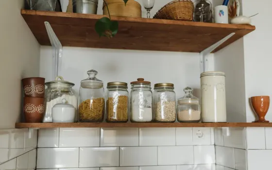 Glass jars of pasta, spaghetti, flour and oats on a wooden shelf above white metro tiles