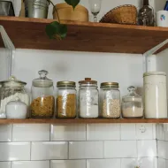 Glass jars of pasta, spaghetti, flour and oats on a wooden shelf above white metro tiles