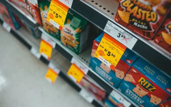 Angled view of yellow Savings This Week stickers clipped to a shelf edge under boxes of snack crackers
