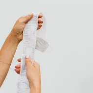 Two hands unravelling a long till receipt against a plain grey background