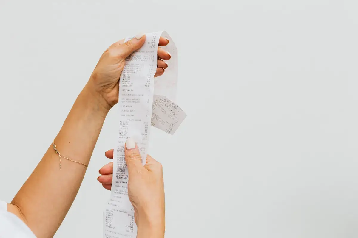 Two hands unravelling a long till receipt against a plain grey background