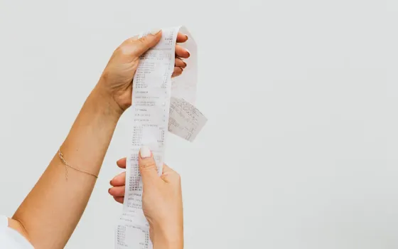 Two hands unravelling a long till receipt against a plain grey background