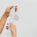 Two hands unravelling a long till receipt against a plain grey background