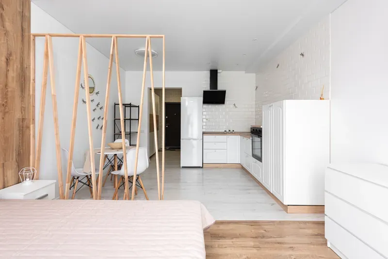 Studio flat with a slatted timber screen between a bed and a white kitchen with dining table