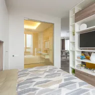 Double bed with grey chevron duvet beside an open shelving unit holding a television and books