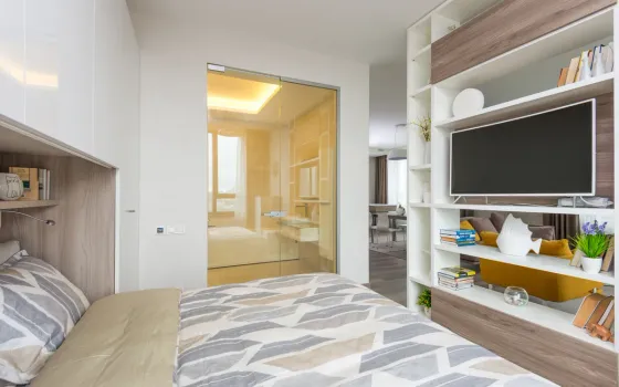 Double bed with grey chevron duvet beside an open shelving unit holding a television and books