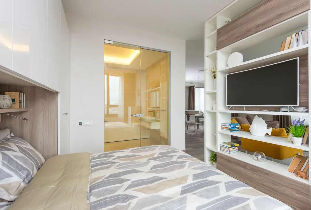 Double bed with grey chevron duvet beside an open shelving unit holding a television and books