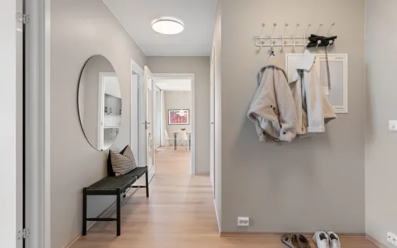 Grey-painted hallway with two coats on a white peg rail, a round mirror and a black bench