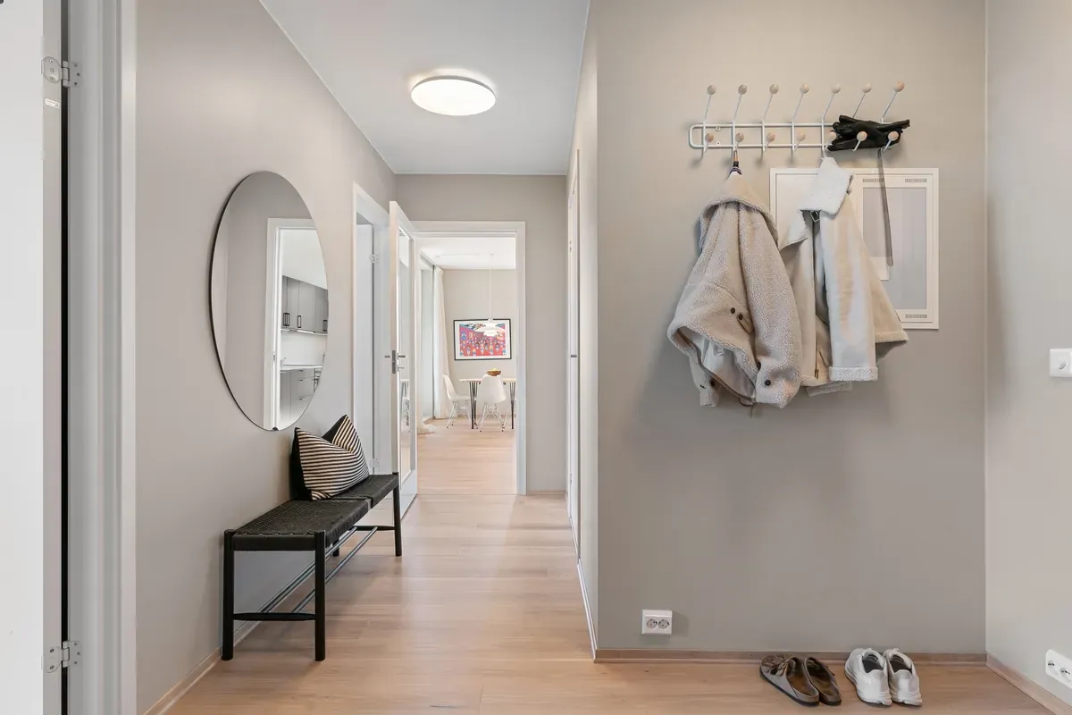 Grey-painted hallway with two coats on a white peg rail, a round mirror and a black bench