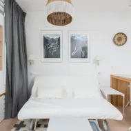 White sofa bed pulled out on castors under two framed prints, grey curtain and a folding chair beside it
