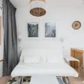 White sofa bed pulled out on castors under two framed prints, grey curtain and a folding chair beside it