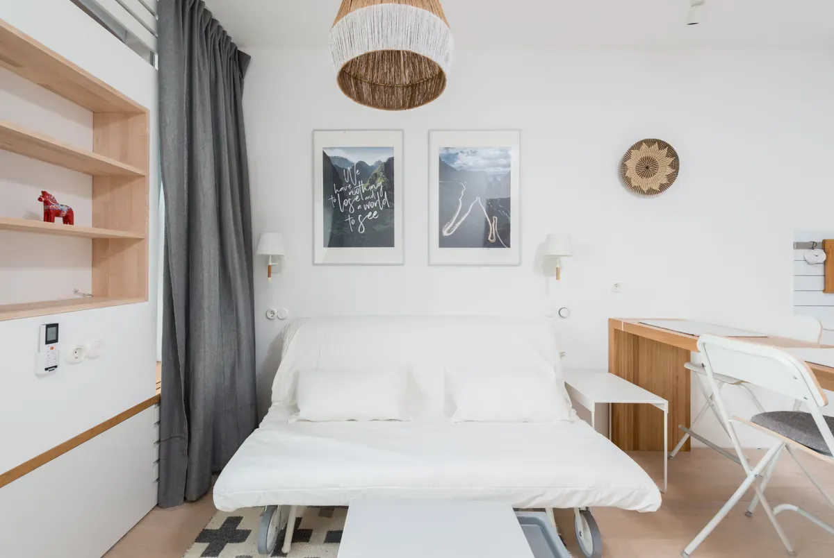 White sofa bed pulled out on castors under two framed prints, grey curtain and a folding chair beside it