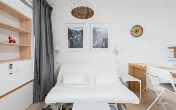 White sofa bed pulled out on castors under two framed prints, grey curtain and a folding chair beside it