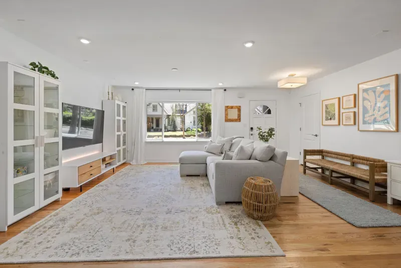 Bright living room with an L-shaped grey sofa, a woven rattan side table and a slatted wooden bench against the wall