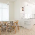 Round white dining table with four wooden folding chairs in a white kitchen with sheer curtains