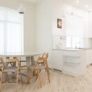 Round white dining table with four wooden folding chairs in a white kitchen with sheer curtains