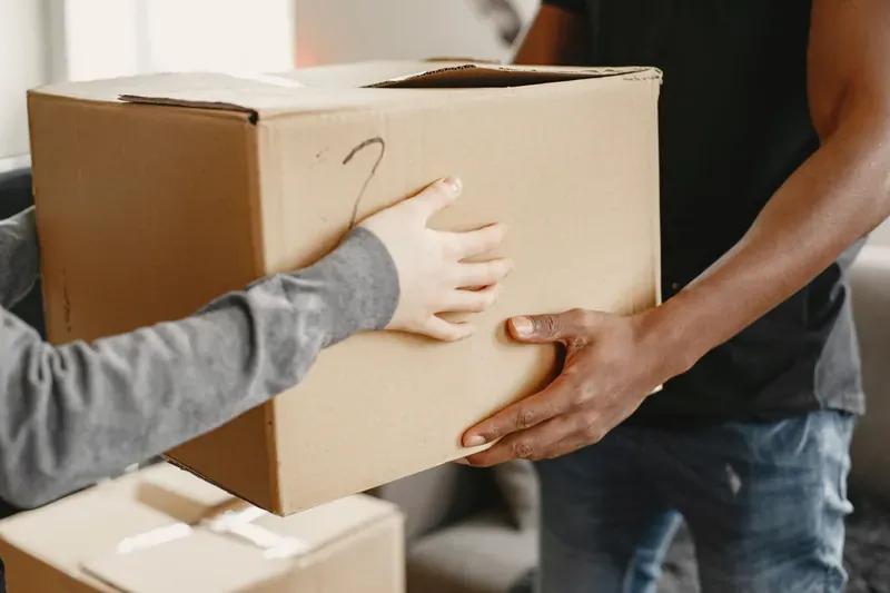 Two people handing over a cardboard box marked with a number two in marker pen, one in a grey sleeve and one in a black T-shirt