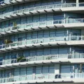 Curved modern apartment block with tiers of glass balconies, metal railings and outdoor chairs stacked in rows