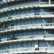 Curved modern apartment block with tiers of glass balconies, metal railings and outdoor chairs stacked in rows