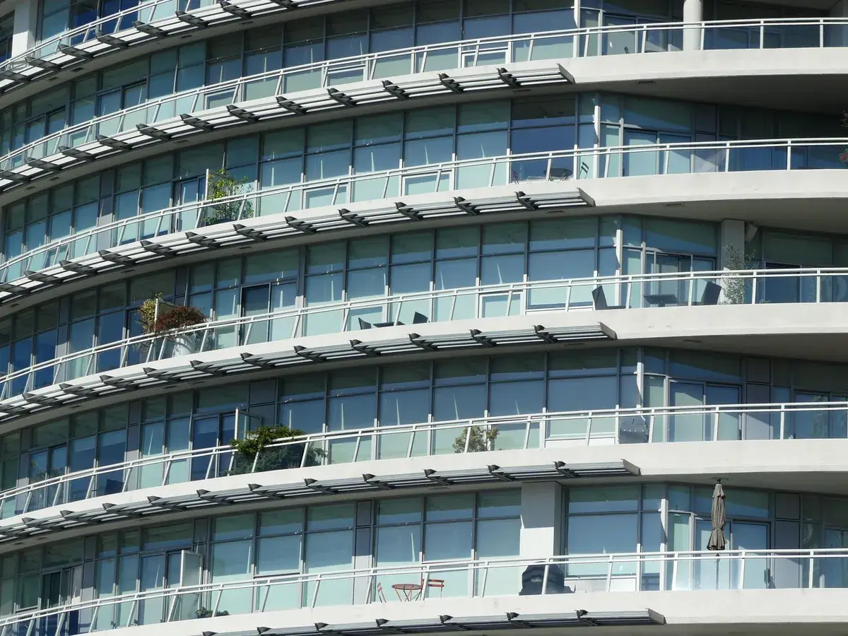 Curved modern apartment block with tiers of glass balconies, metal railings and outdoor chairs stacked in rows